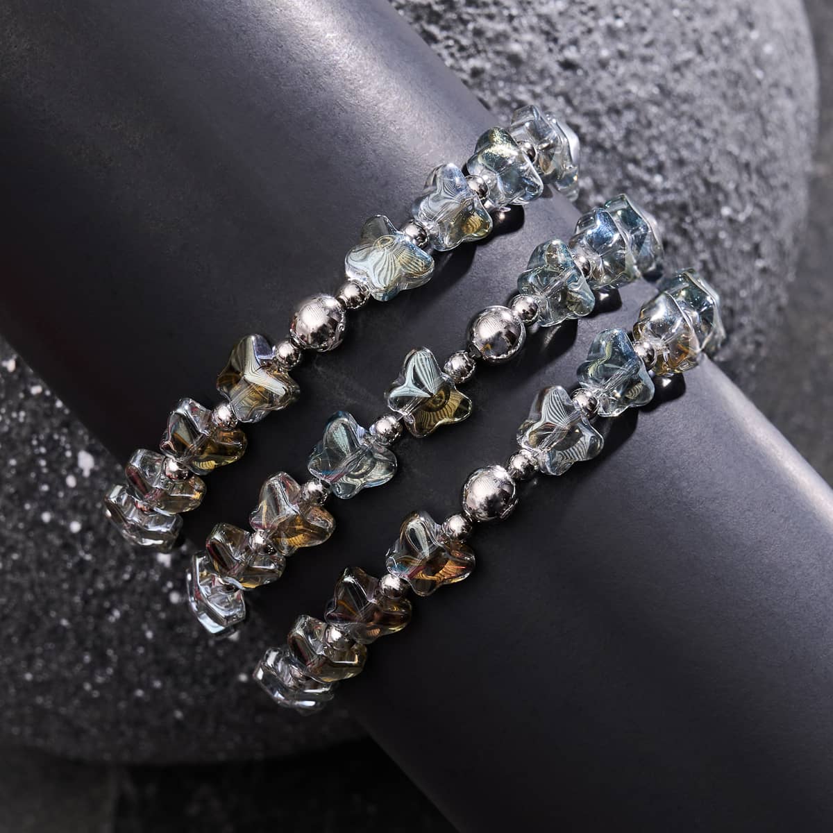 Olive Monarch silver butterfly bracelets with hand-strung beads and stainless steel charms on stretchable elastic cords displayed on textured black surface by NOGU